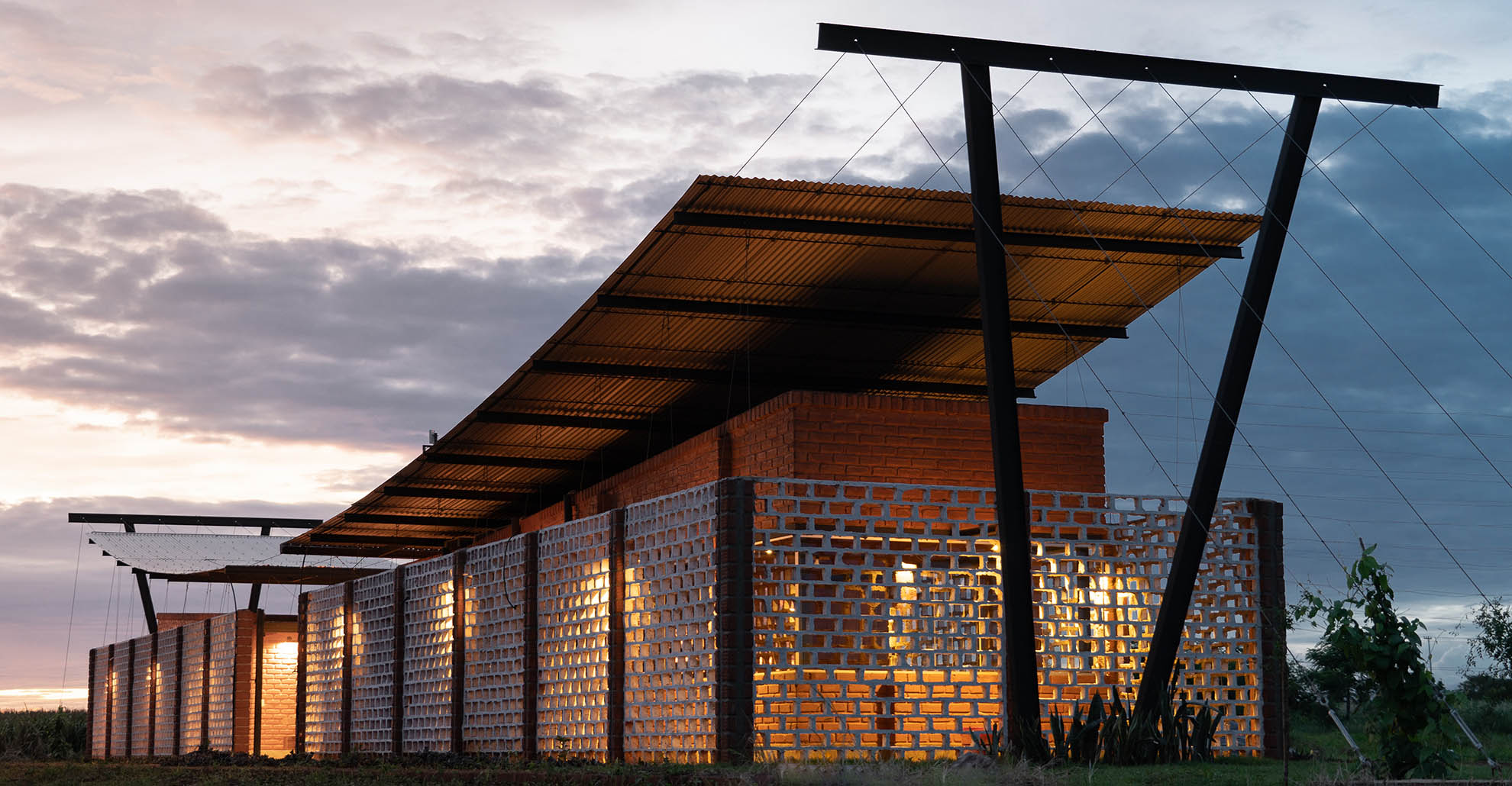 Fachada iluminada de la Oficina Nordeste Curuguaty, en la que destaca el uso de ladrillos y la reutilización de recursos locales en su diseño.