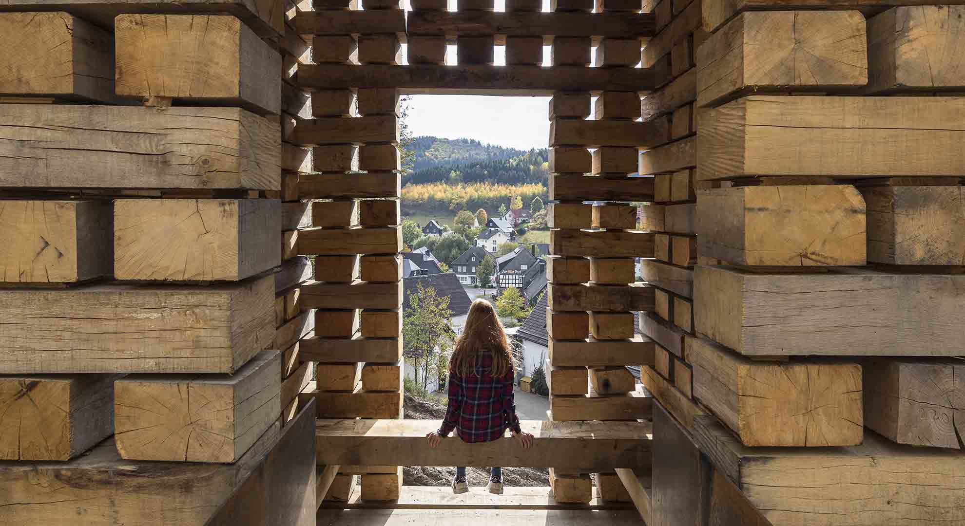 Espacio arquitectónico construido con madera apilada, que enmarca una vista panorámica y resalta la conexión entre arquitectura y sostenibilidad.