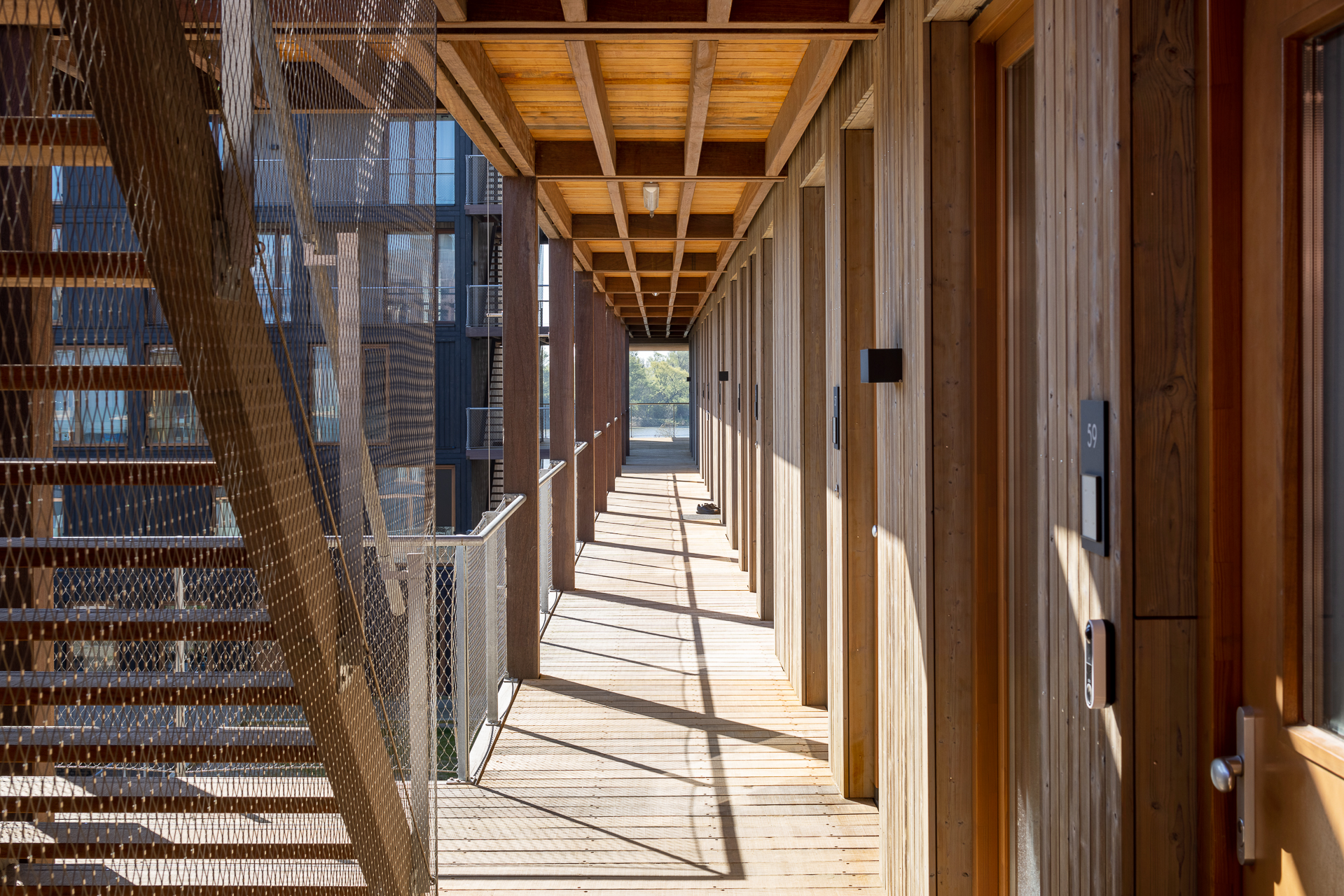 Pasillo de acceso del edificio Juf Nienke con acabados de madera natural, ejemplo de diseño sostenible y vivienda responsable.