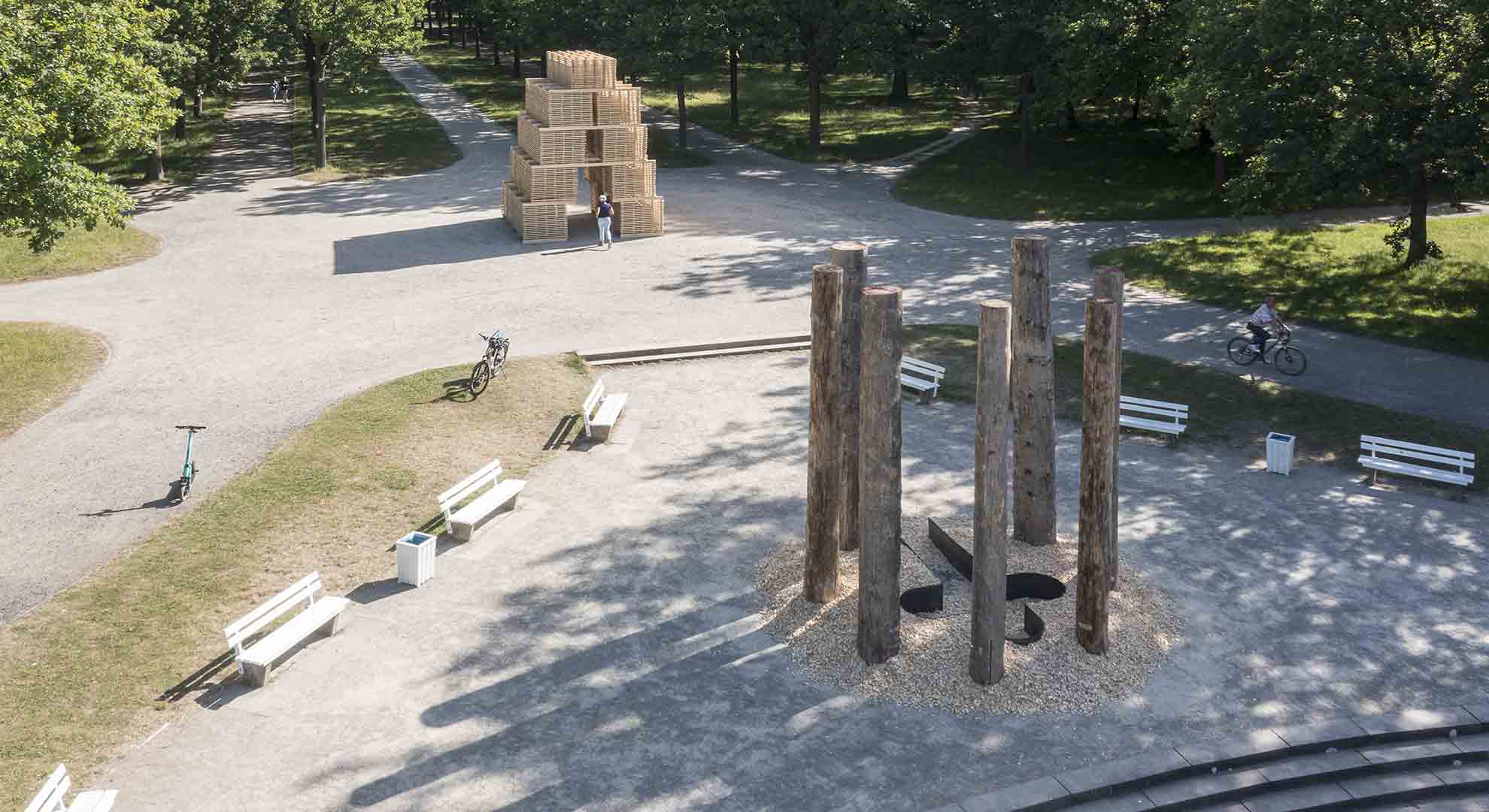 Instalación arquitectónica en un parque urbano con elementos de madera y estructura geométrica, en la que destaca la relación entre arquitectura y sostenibilidad.